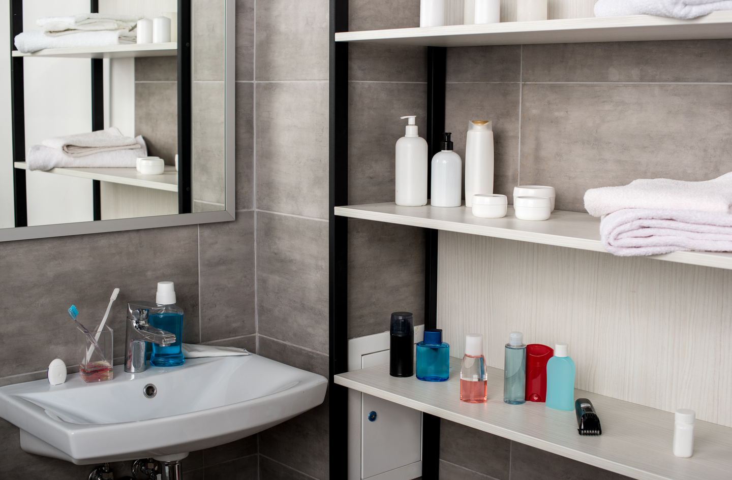 A white bathroom sink with toiletries alongside a wall-mounted shelving unit at counter height demonstrating accessible small bathroom storage