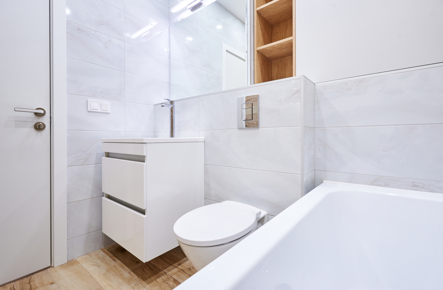 A modern bright bathroom with a wall-mounted toilet and a wooden recessed shelf built directly into the wall above the toilet, showing how to use vertical space in a small bathroom storage layout without reducing floor clearance.