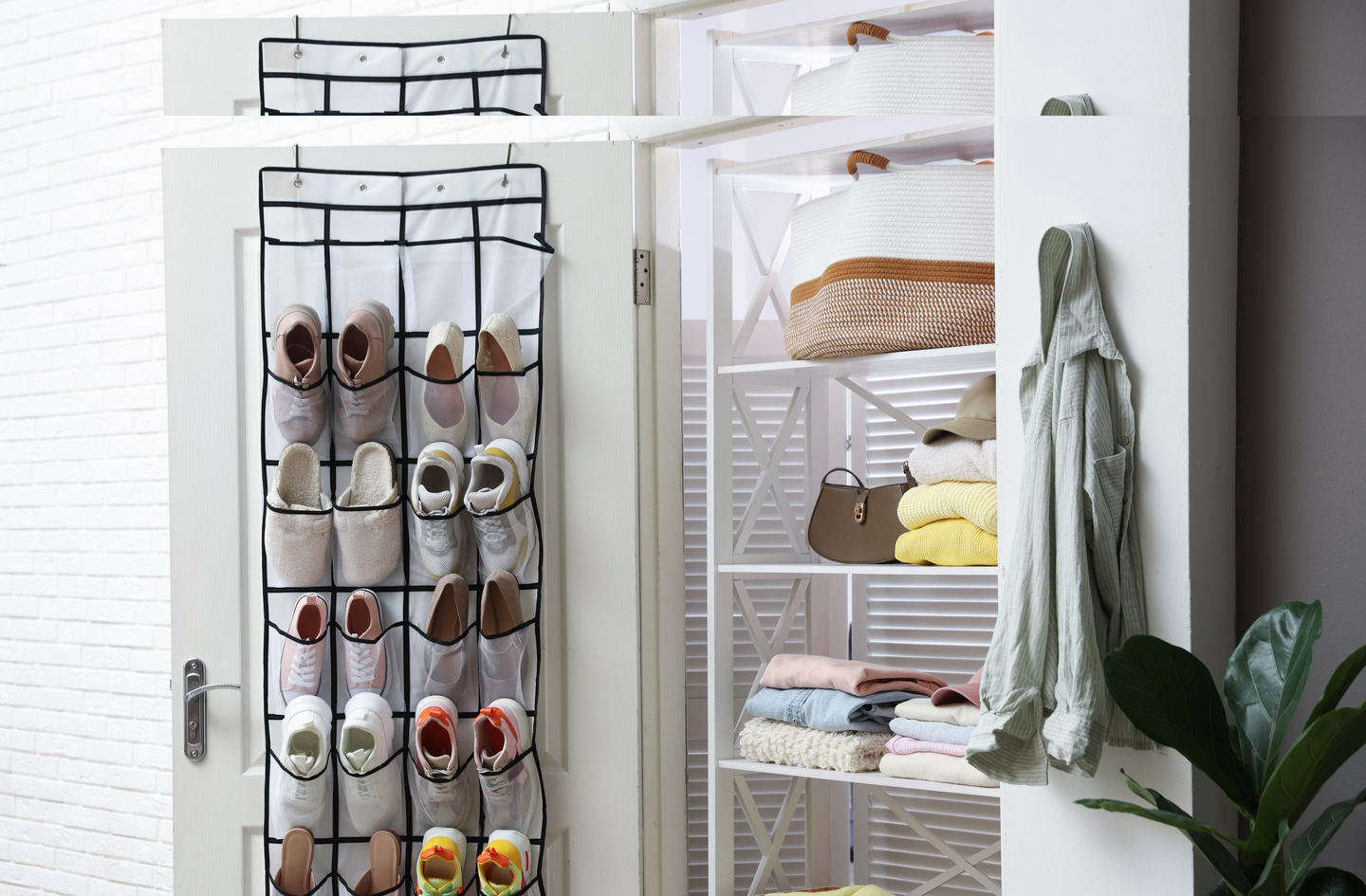 An over-the-door hanging shoe organizer filled with several styles of footwear is mounted on an open white door beside a white shelving unit holding folded clothes and bags.