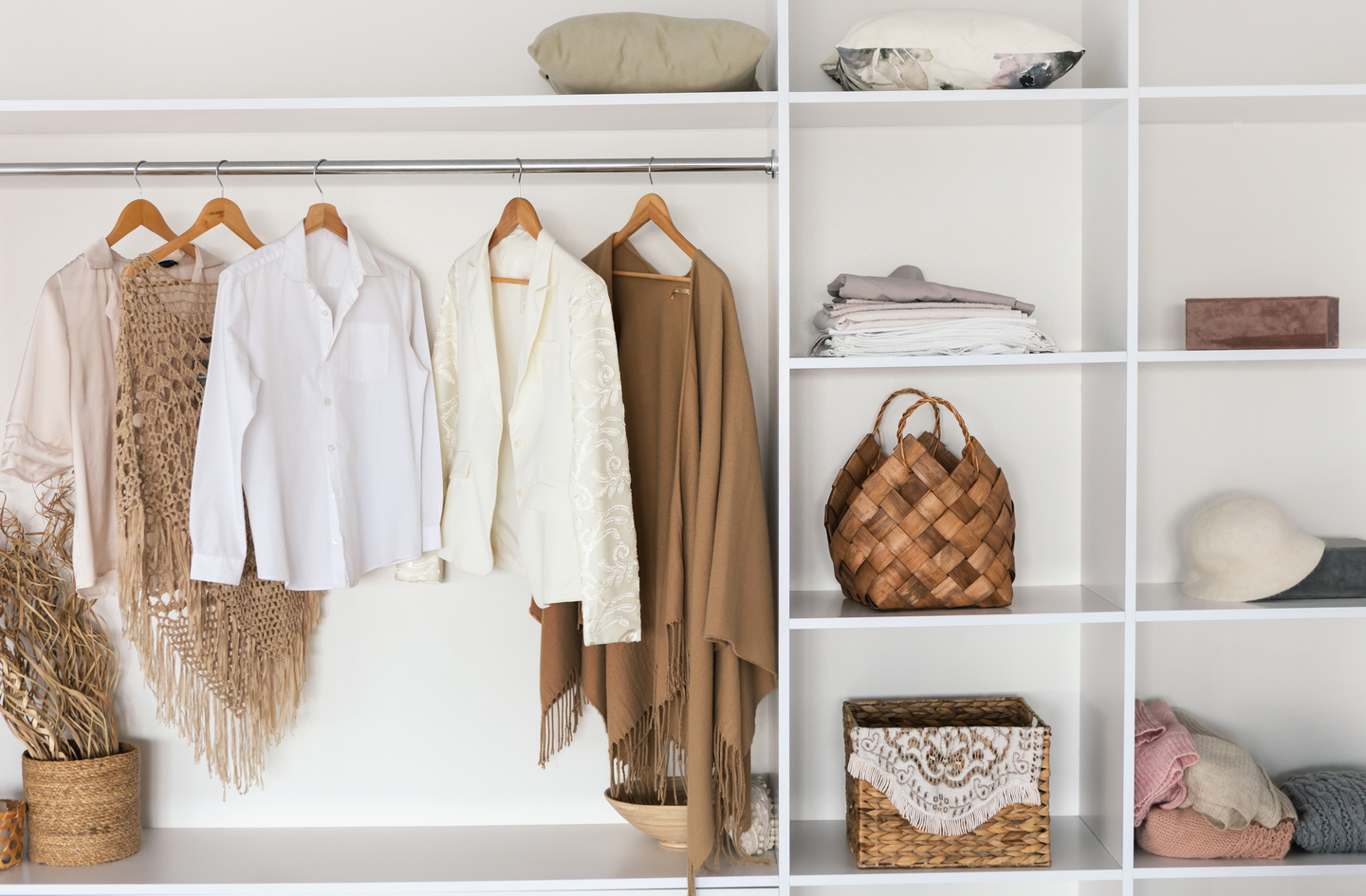 A bright walk-in closet with neutral clothing on wooden hangers beside open shelves of folded textiles and woven baskets, with hanging and folded storage kept against the walls.