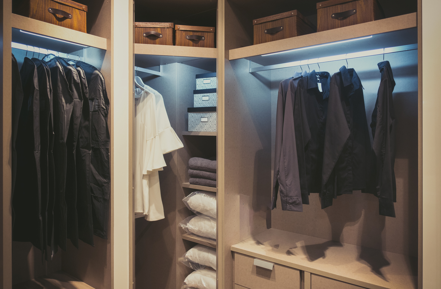 Small walk in closet organization ideas in practice: a closet divided into three sections, with hanging clothes on the left and right and neatly stacked folded items and storage boxes on lit shelves in the middle.